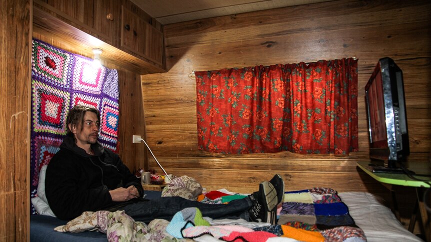 Luke Skinner at home in his caravan watching TV in bed.