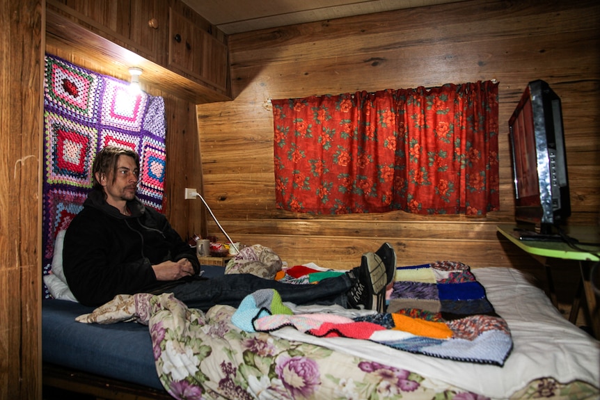 Luke Skinner at home in his caravan watching TV in bed.
