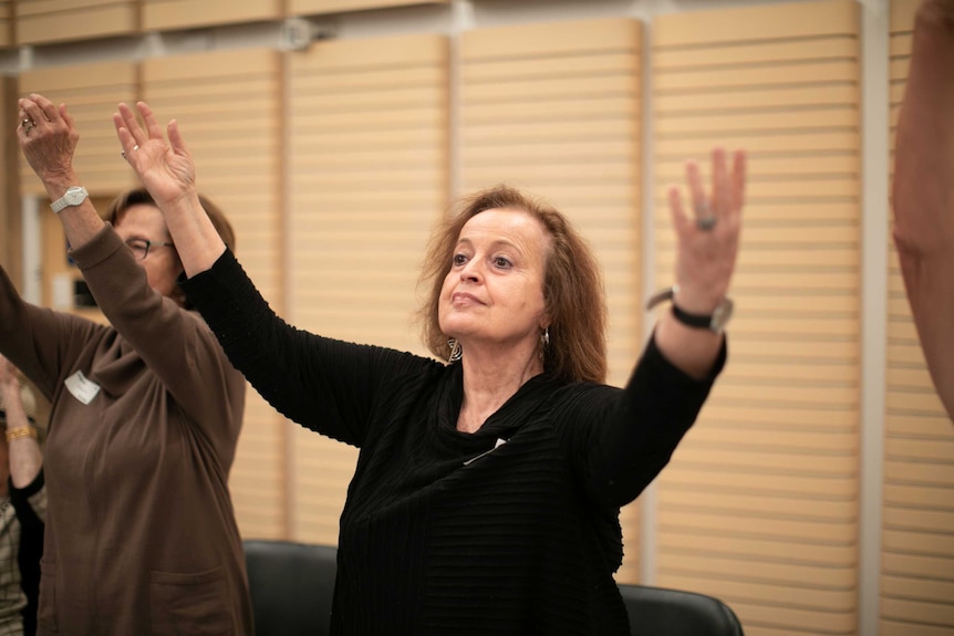 Mary Colbert raises her arms in the air above her head.