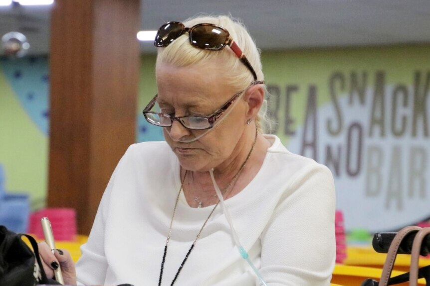 Lyn has tubes in her nose while playing bingo.