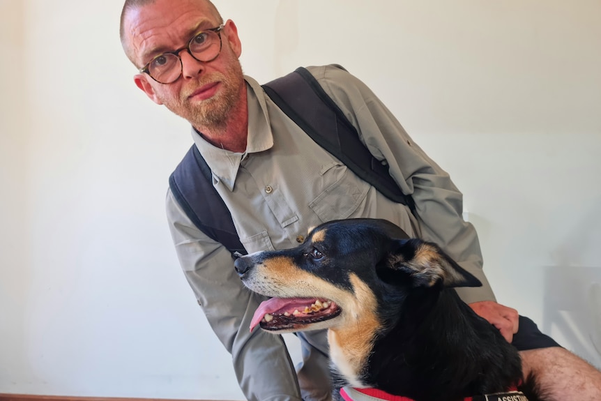 A man in glasses hugs a dog.