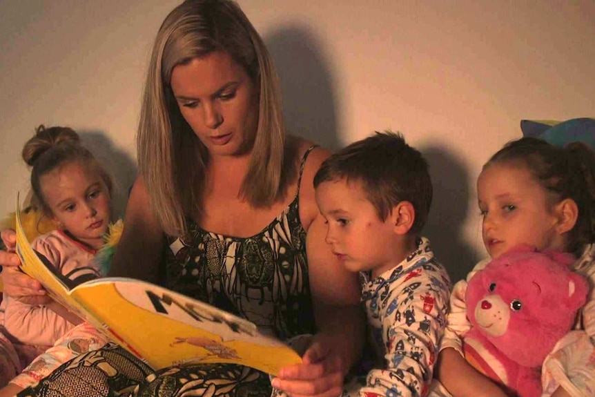 Corinne Merrigan reads from a picture book as her children listen.