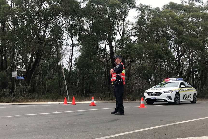 A policeman stands next to a police car on a road through a forest