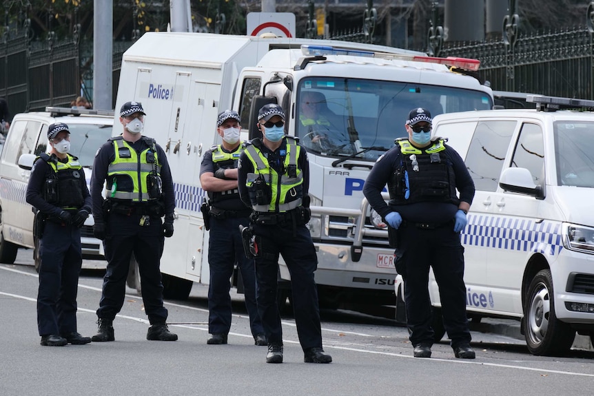 Six Victoria Police officers wearing masks stand near a police van.