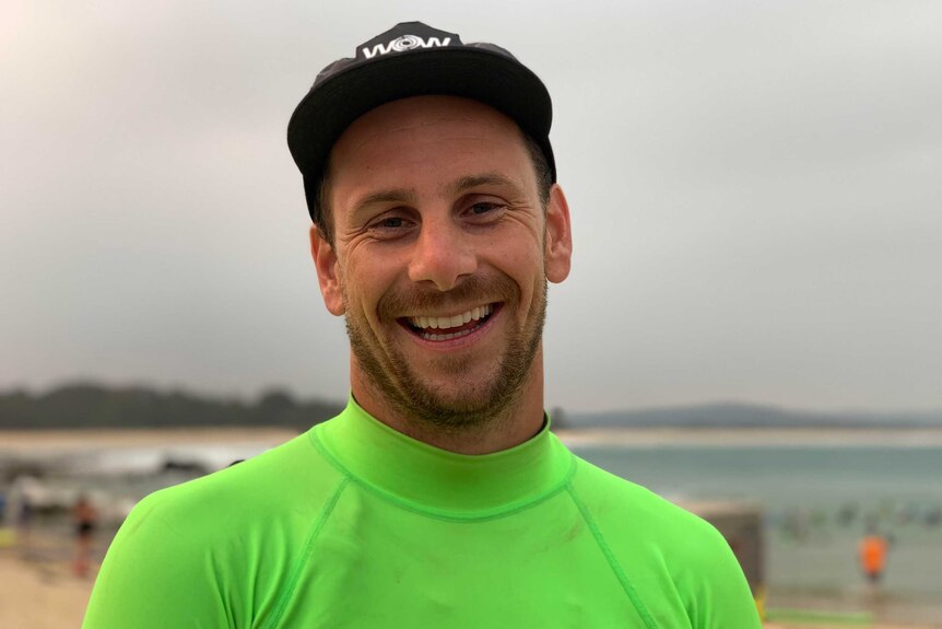 A man in his late thirties, early forties, wearing a neon green wetsuit and smiling widely at the camera.