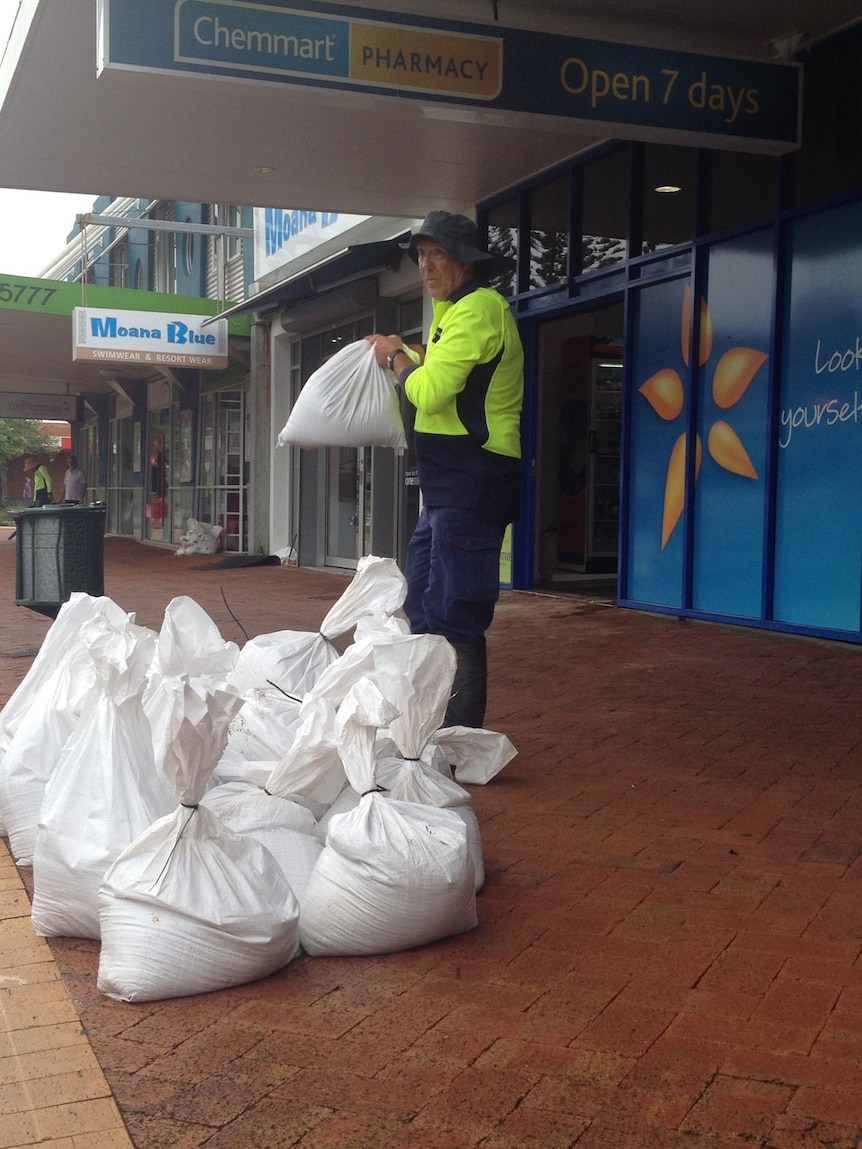 Worker with sandbags outside pharmacy after flash flood in James Street in Yeppoon