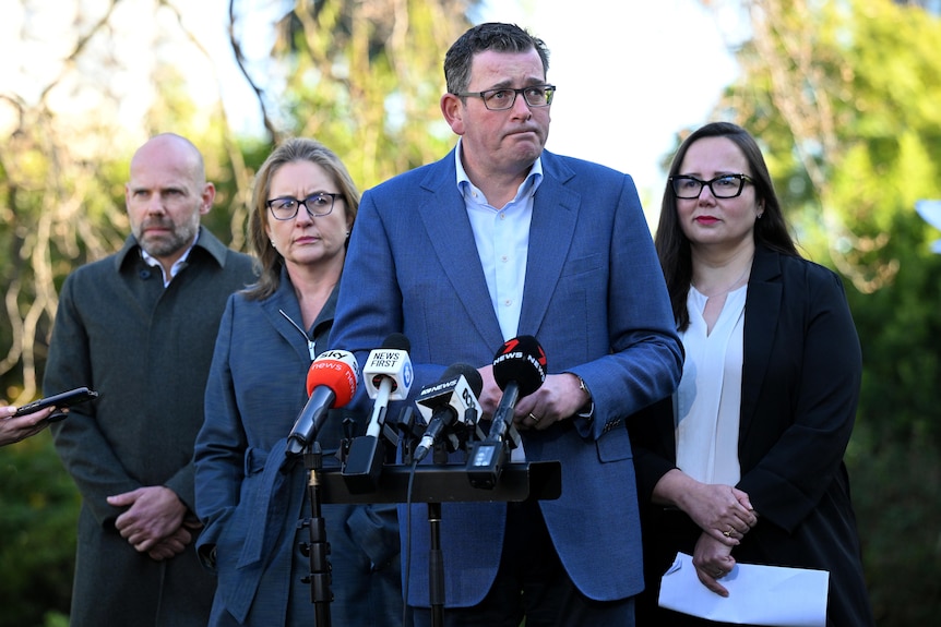 Daniel Andrews viste un traje azul y una camisa blanca y frunce el ceño mientras mira fuera de cámara.