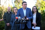 Daniel Andrews wears a blue suit and white shirt and frowns while looking off camera.