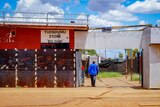 A man walks into a tin shed with a sign on it that says 'Yuendumu Store'