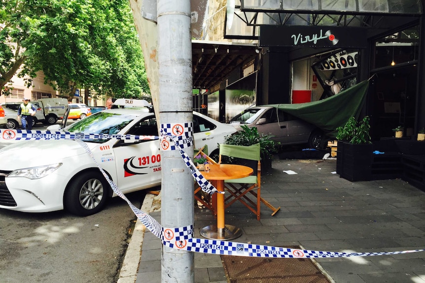 A car inside the smashed shop front of a cafe next to a damaged taxi with police tape surrounding the scene