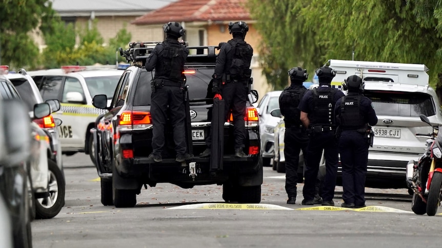 Armed police in vests and helmets and police vehicles in a suburban street