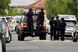 Armed police in vests and helmets and police vehicles in a suburban street