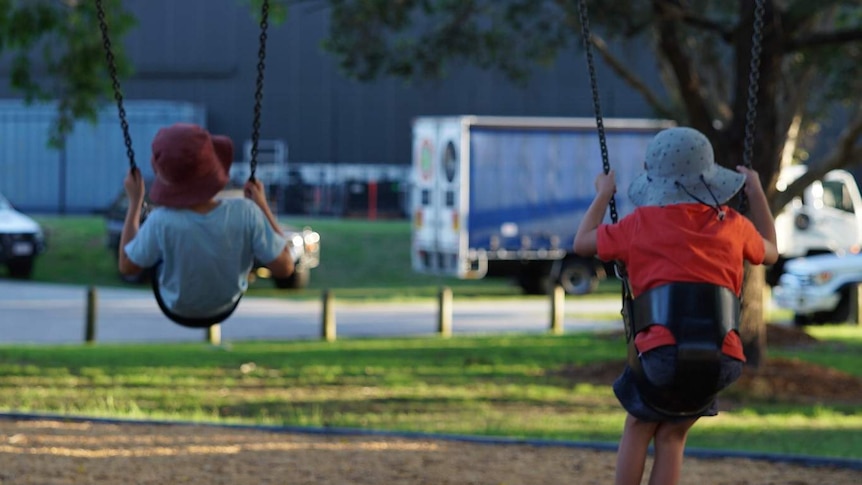 Two anonymous children play on swings in a park.