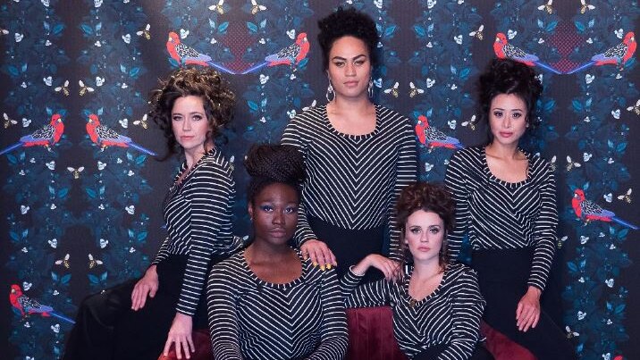 Five women of different racial backgrounds wear the same black and white striped top and wear their hair in a beehive
