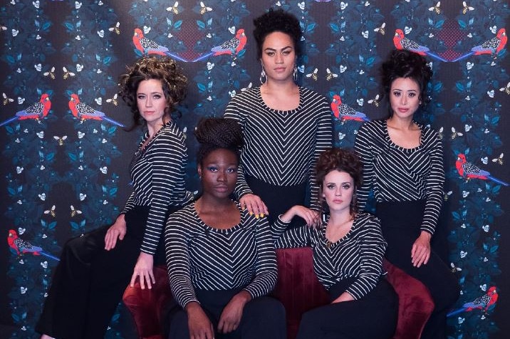 Five women of different racial backgrounds wear the same black and white striped top and wear their hair in a beehive