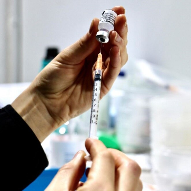 A female hand holds a needle inserted into a vial of a COVID-19 vaccine