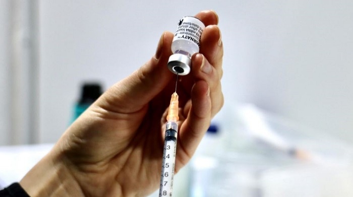 A female hand holds a needle inserted into a vial of a COVID-19 vaccine