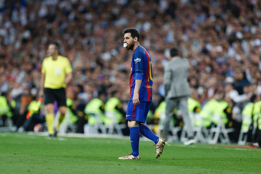 Lionel Messi walks with a bandage in his mouth during El Clasico