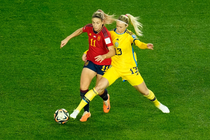 Two female soccer players battling for the ball on field.