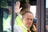 Bill Shorten waves to the media from inside the glass cab of large forklift.