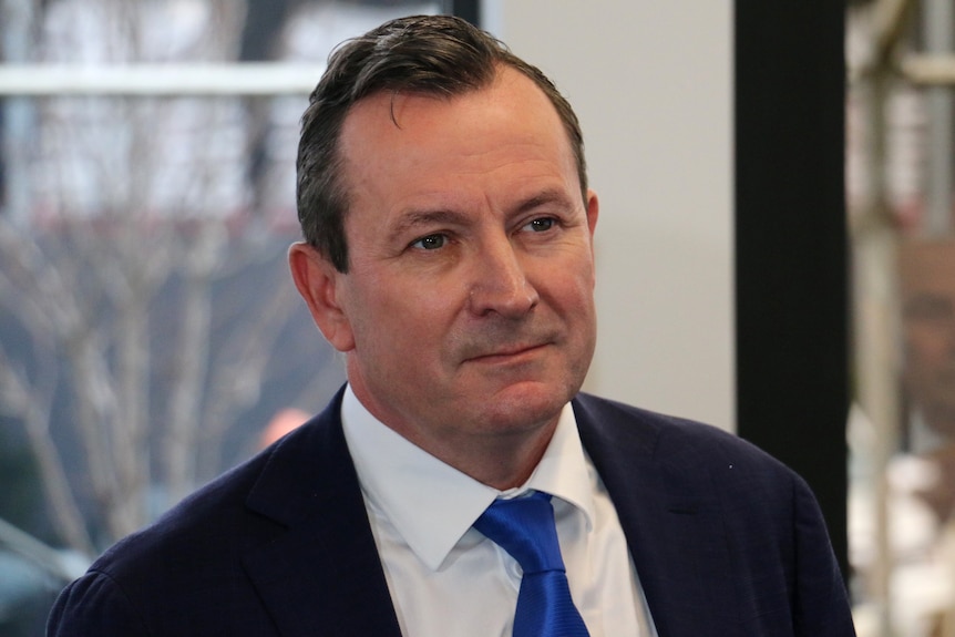 A head and shoulders shot of a smiling WA Premier Mark McGowan wearing a dark suit, white shirt and blue tie.