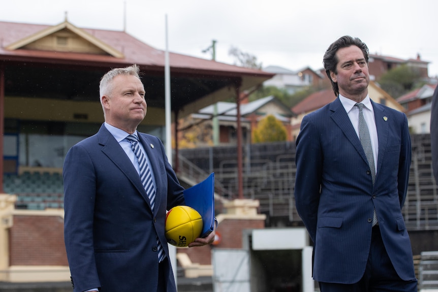 Two men in suits stand on a football field