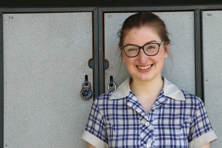 A young girl in a school uniform stands in front of some school lockers.