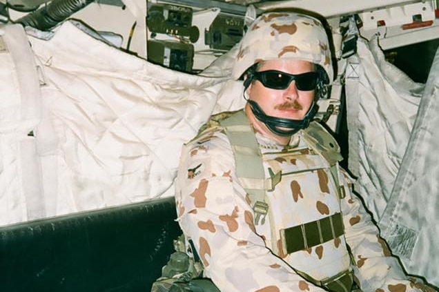 David Gillard sits in the back of an army vehicle in his army uniform.