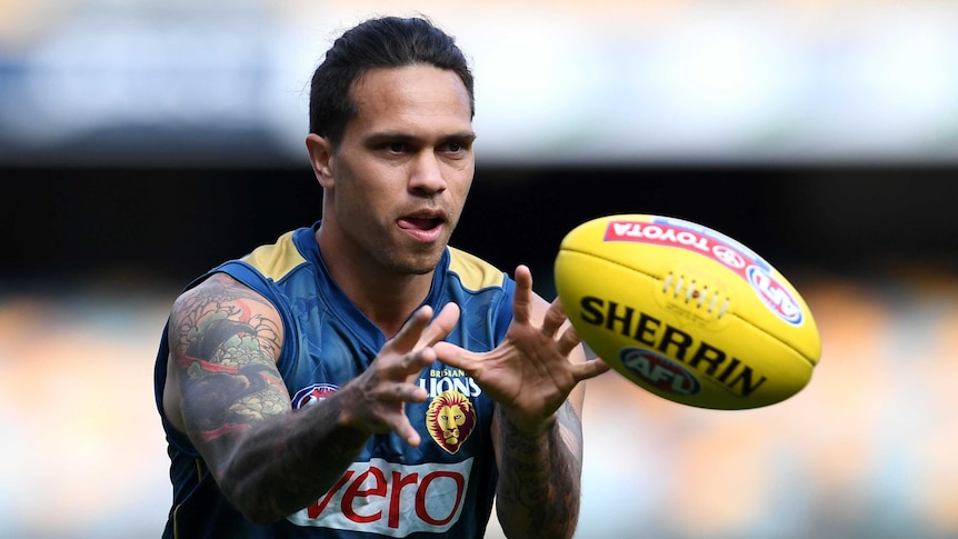 An AFL player holds his hands out to grab the ball at training.