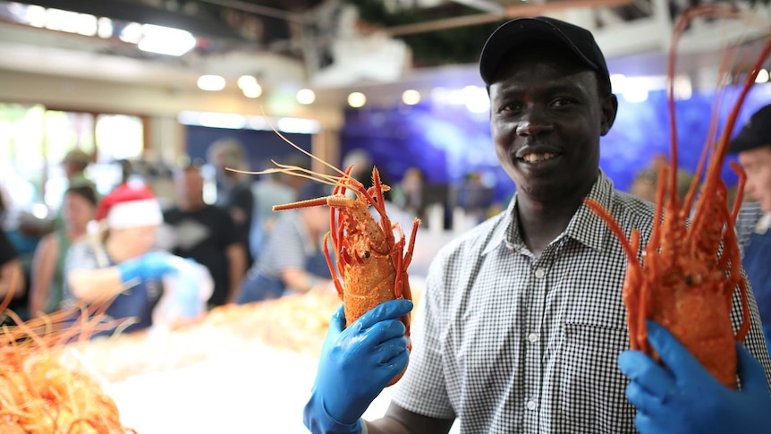 A man holds up two large cooked crayfish inside a shop.