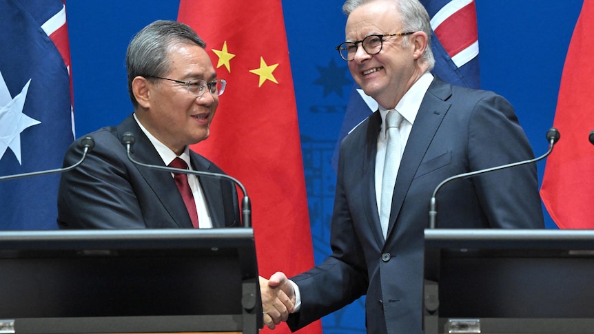 Chinese Premier Li Qiang and Australia's Prime Minister Anthony Albanese shake hands while standing in front of national flags.