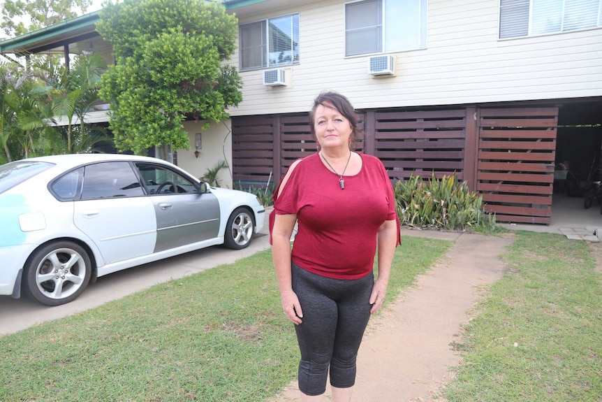 A woman stands in a driveway in front of a car and a house