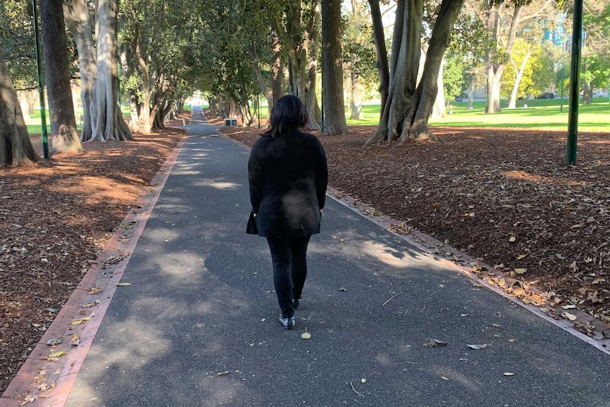 A woman dressed in black walks down a path in a park.