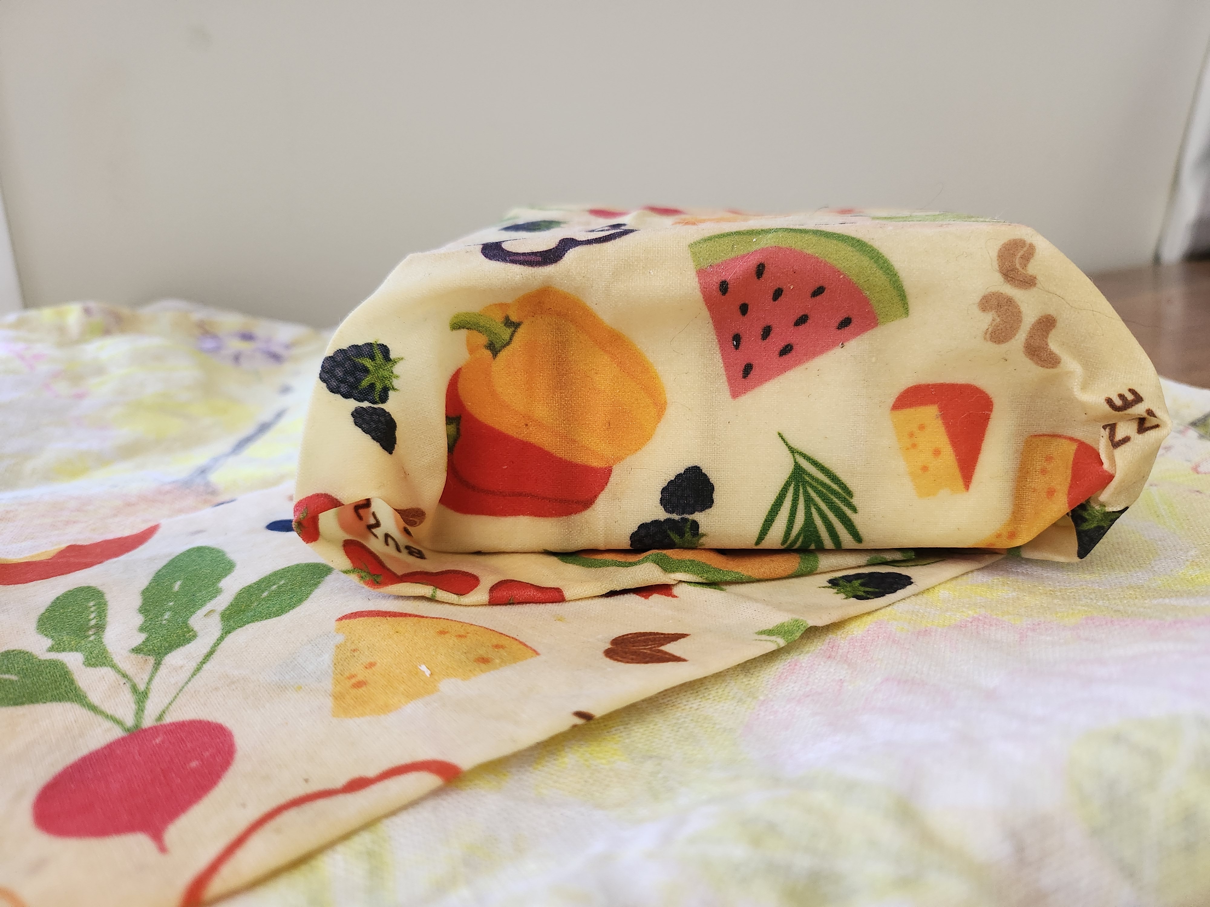 A beeswax wrap patterened with food items covers a box.