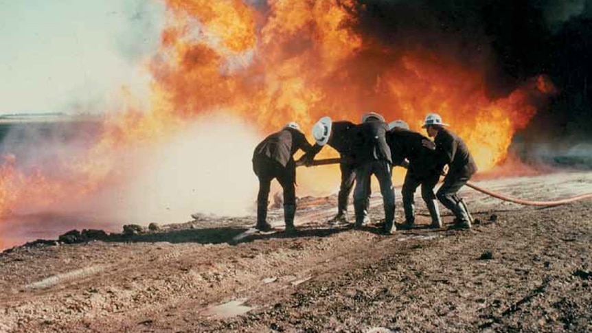 Firefighters in the foreground with a wall of flames behind them