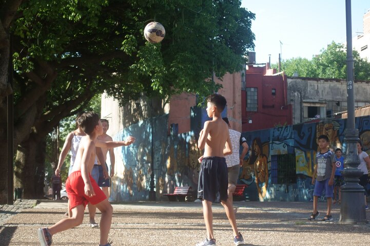 Kids playing football on a dusty street.