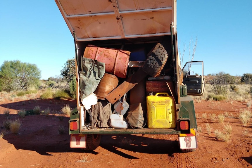 A full trailer on a dirt road containing various rubbish including tyres and jerry cans.