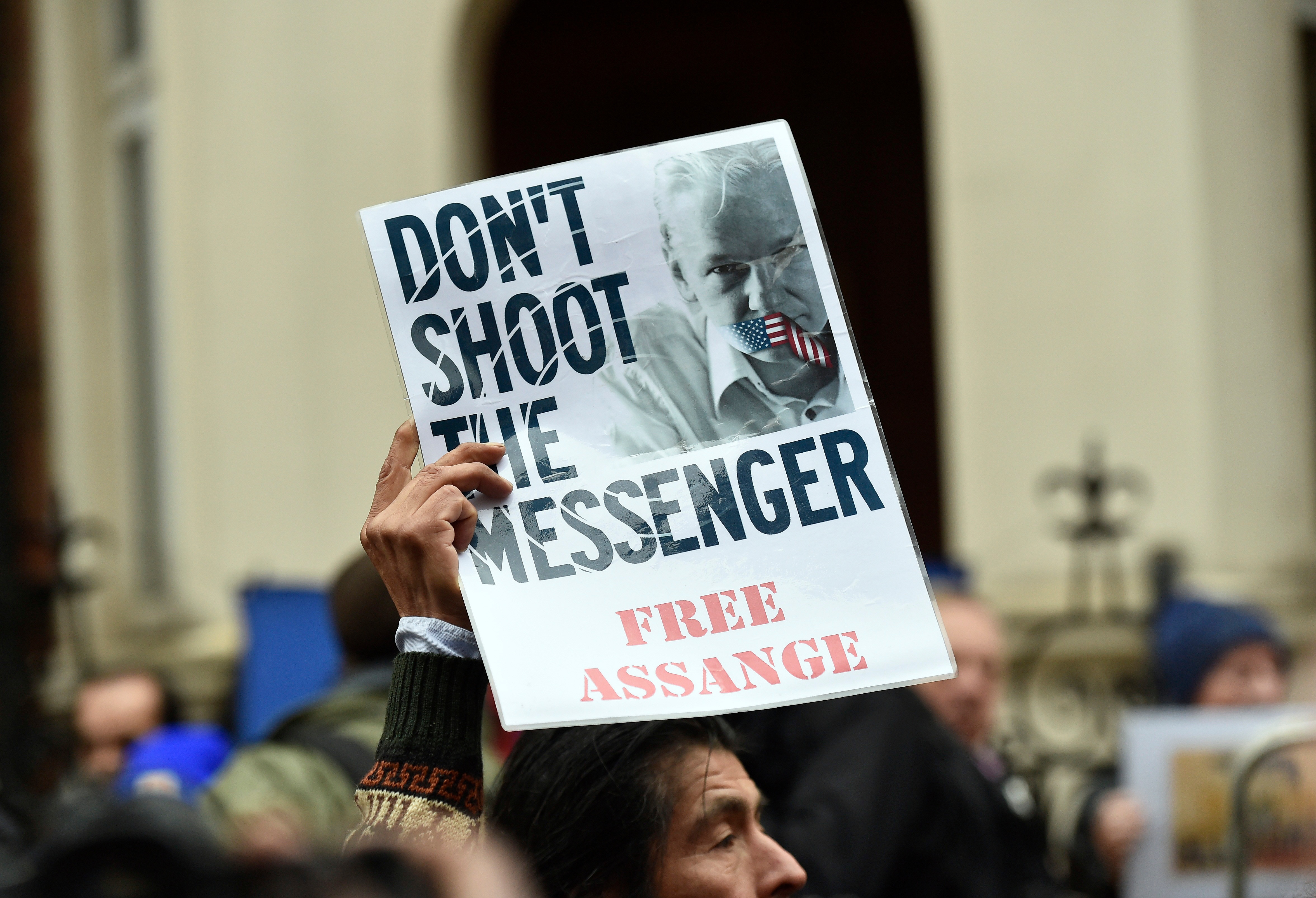 A man holds up a sign that reads Don't Shoot the Messenger, Free Assange with Julian's mouth taped over with the US flag