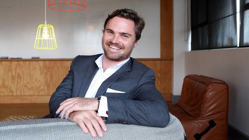 A man with a beard, wearing a blue suit, sitting on a couch.