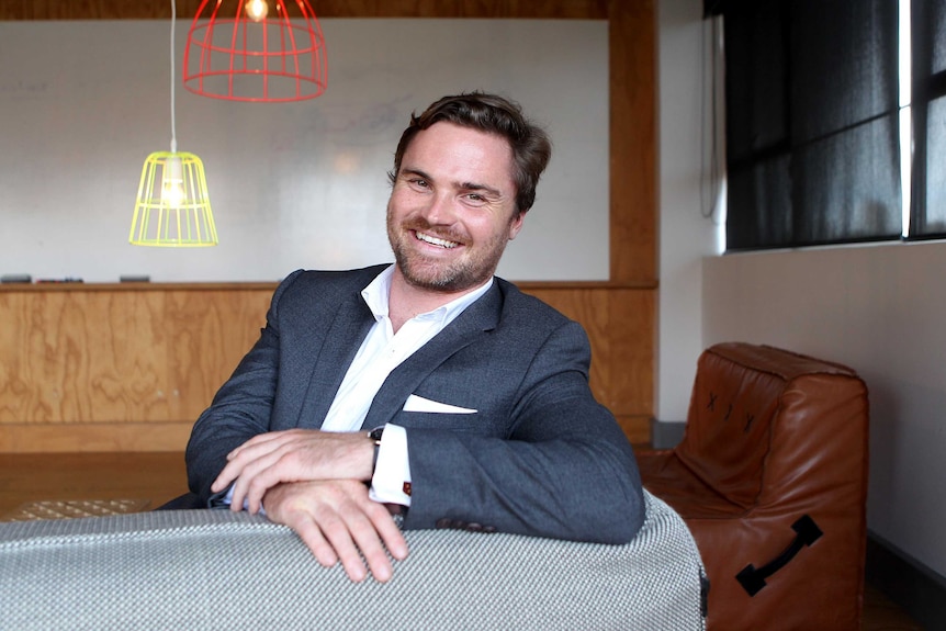 A man with a beard, wearing a blue suit, sitting on a couch.