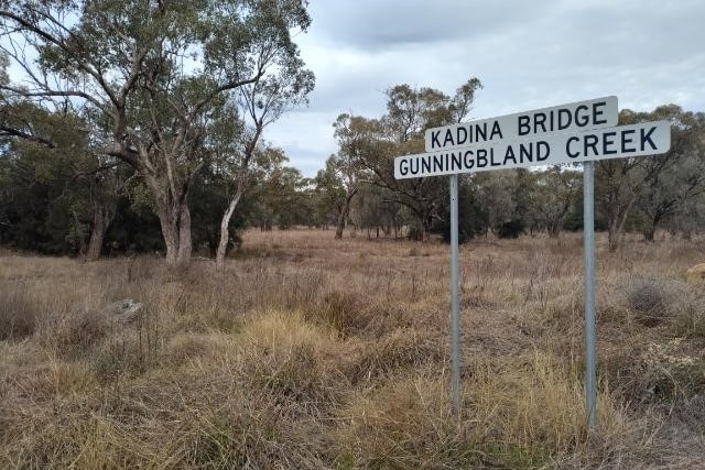 Sign for Gunningbland Creek with dry grass and no water.
