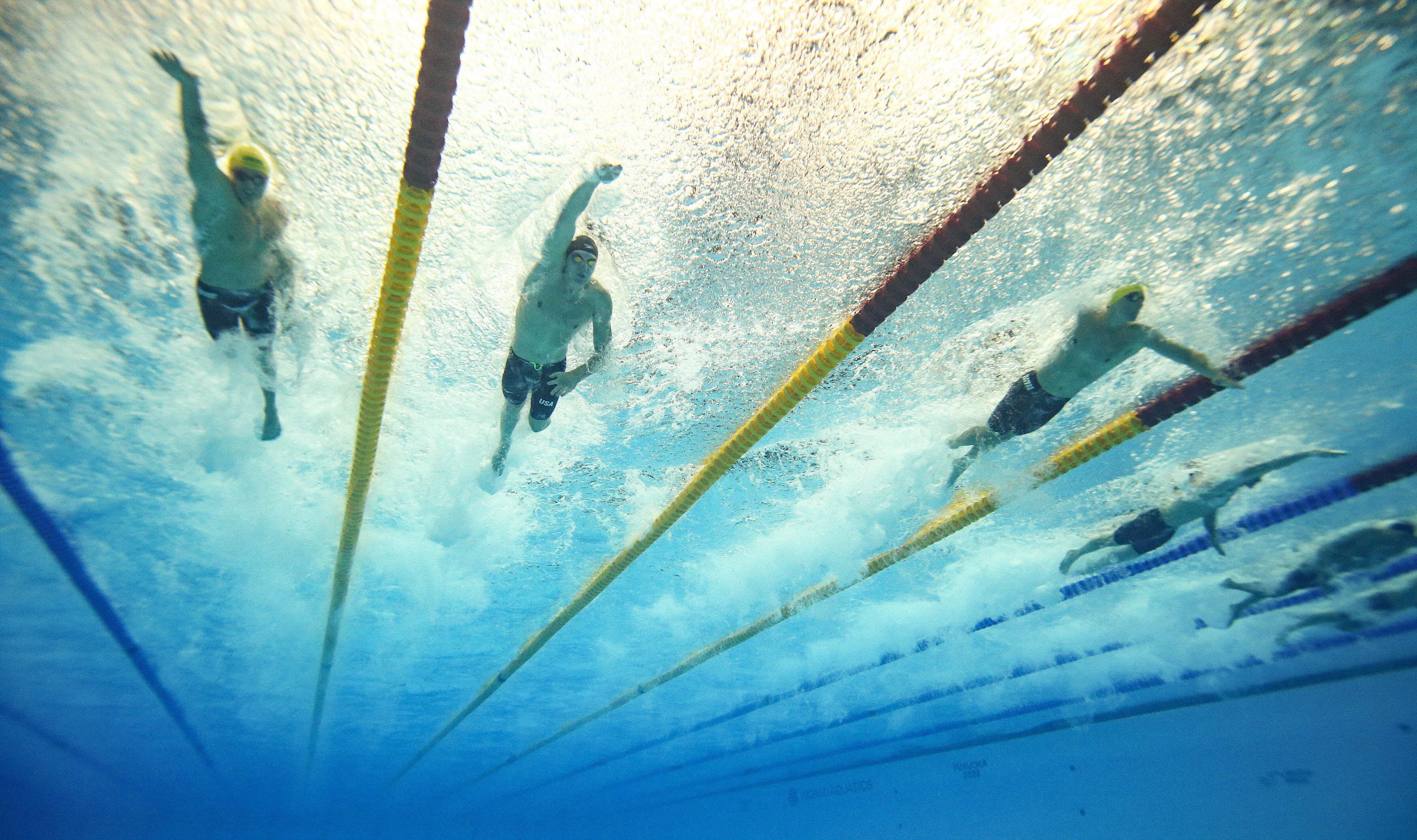 Swimmers seen from below in the pool, frothy water, yellow and dark coloured lane dividers.