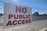 A white sign with red writing an a security fence that states "No public access" in red.