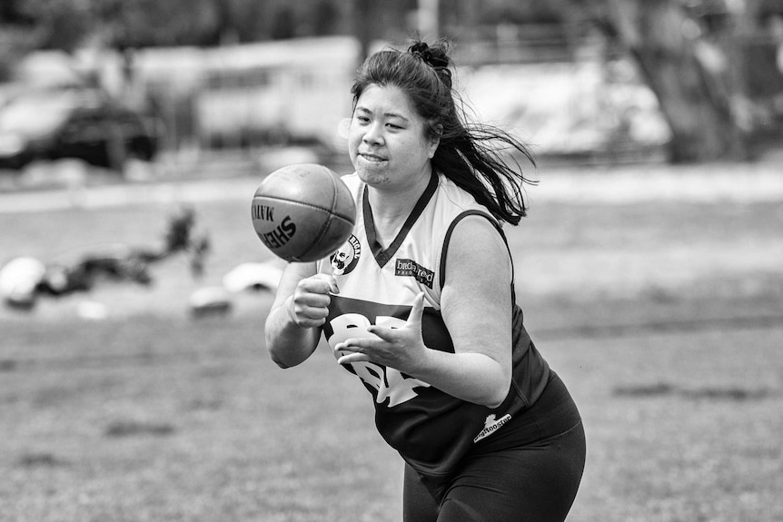 A woman handballs an Aussie Rules ball.