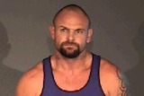 A police photo of Adam Beniamini, a muscular man with tattoos wearing a blue and white singlet.