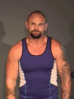 A police photo of Adam Beniamini, a muscular man with tattoos wearing a blue and white singlet.