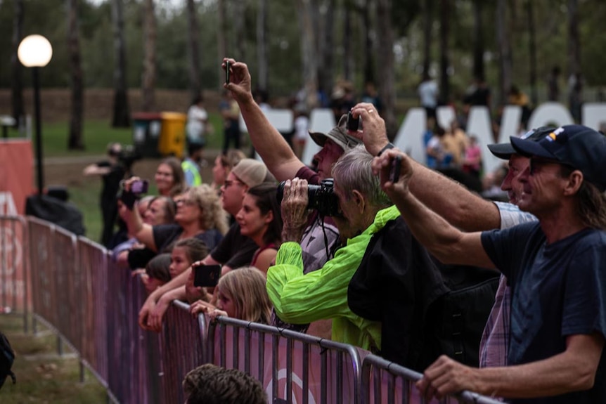 A crown leans over railing at a concert taking photos