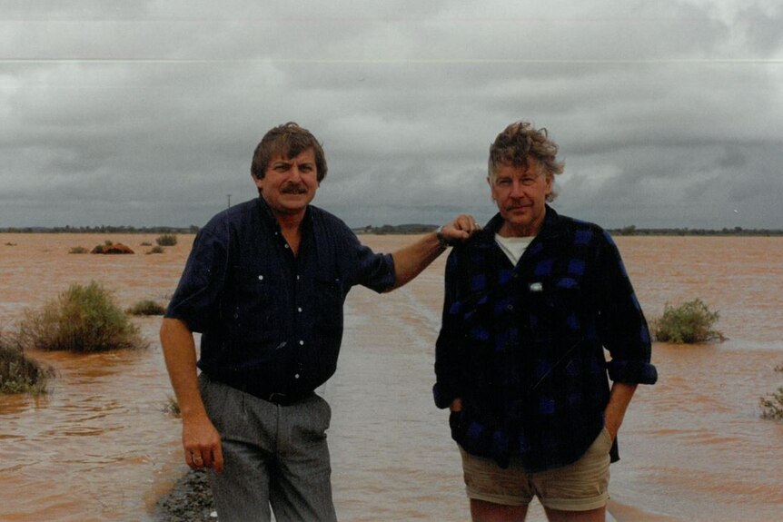 Two men standing next to floodwaters in outback location.  