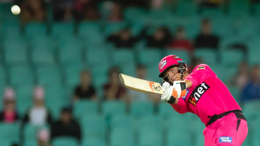 Sydney Sixers batsman Josh Philippe sends a white cricket ball flying through the air.