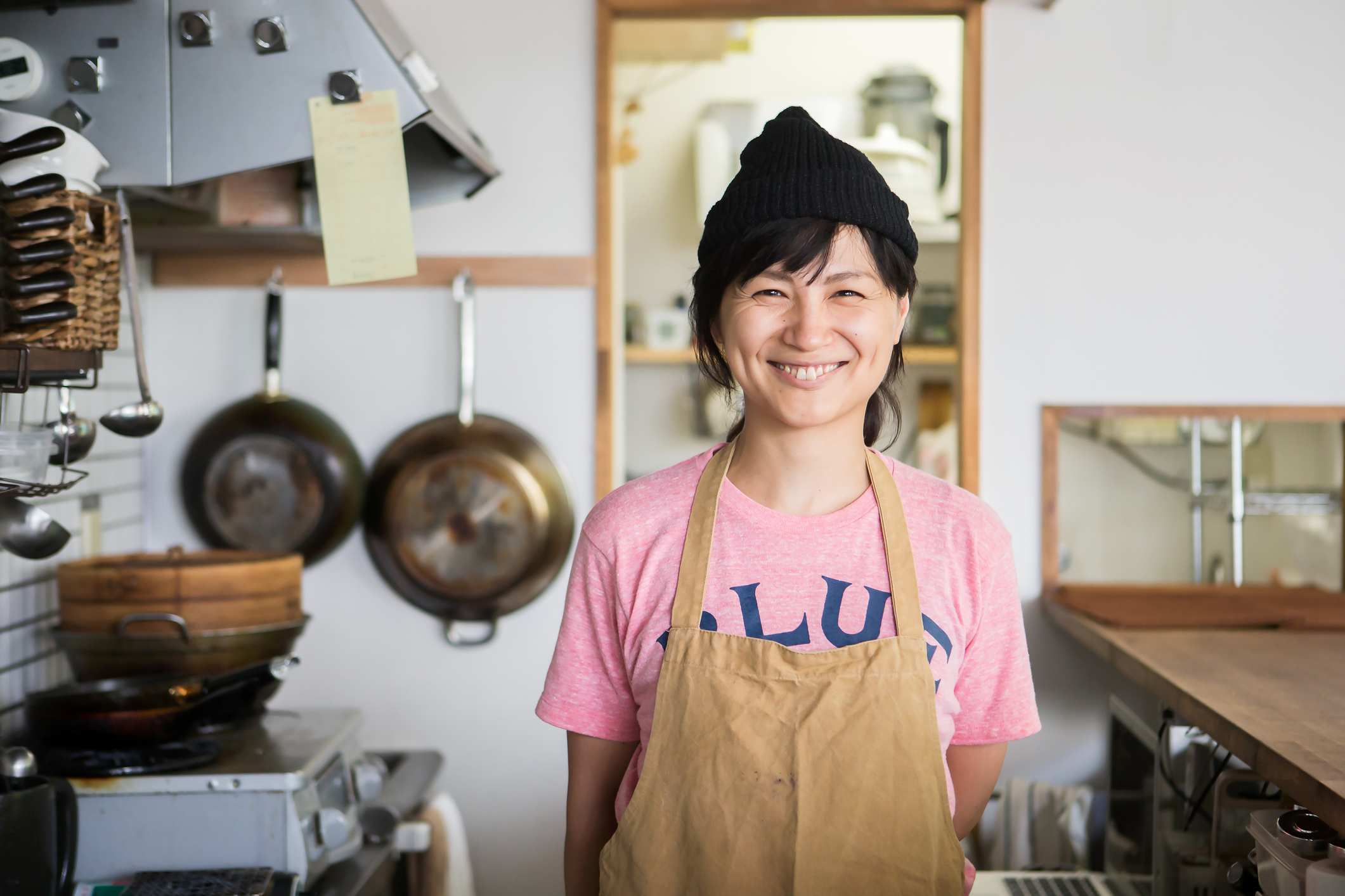 Woman with black hair smiling into the camera standing in kitchen with apron on